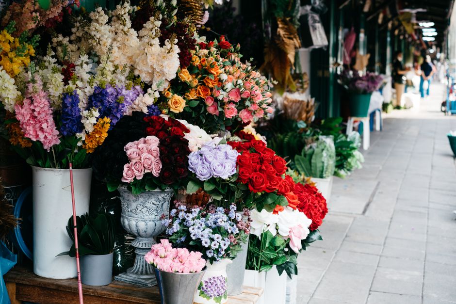 A vibrant display of fresh floral arrangements outside a florist shop, showcasing a variety of roses in shades of pink, red, lavender, and cream, as well as hydrangeas and other mixed flowers in full 
